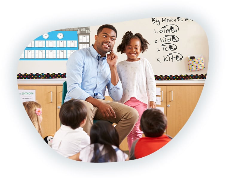 Photo of a a teacher in front of his students, holding his ear demonstrating listening skills.